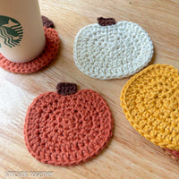 close up of crochet pumpkin coasters, one of the coasters has a starbucks cup sitting on it