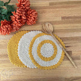 3 round crochet dishcloths on a counter with a wooden spoon laying across them