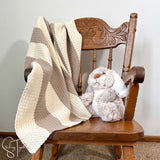 striped crochet blanket draped on a small rocking chair with a stuff bunny on the seat