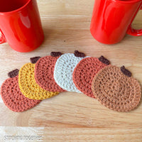 crochet coasters in a pumpkin shape spread out from being stacked and sitting next to two red mugs