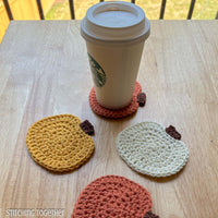 pumpkin crochet coaster with a disposable coffee cup sitting on it and other coasters laying near 