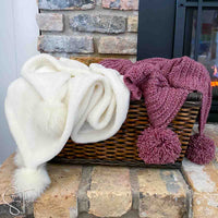 white blanket and a red crochet christmas blanket in a basket next to a fireplace