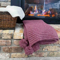 folded christmas crochet blanket with pom poms on the hearth of a fireplace