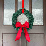 green crochet wreath with a big red bow hanging on a front door