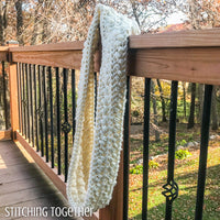 chunky crochet infinity scarf hanging on a deck post