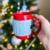 hand holding a red mug with a light blue mug cozy