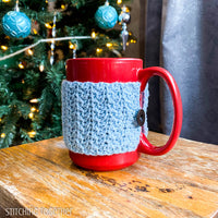 reg mug with blue crochet coffee cup cozy on a table