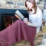 lady reading a book while draped in a marled crochet blanket next to a fireplace