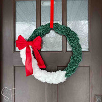 green and white crochet wreath with a big red bow hanging on a front door