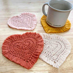 4 crochet heart coasters with fringe and a mug sitting on one of the coasters