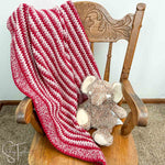 red striped crochet baby blanket draped on a small rocking chair with a stuff elephant sitting on the chair