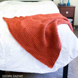 orange crochet throw draped on the end of a bed