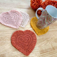 a mug sitting on a crochet heart coaster with other coaster laying nearby