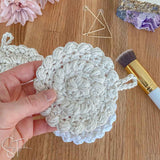 hand holding a crochet face pad with accessories in the background